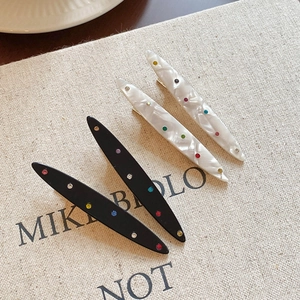 Lot de barrettes en acrylique chic avec strass colorés sur un tissu beige texturé