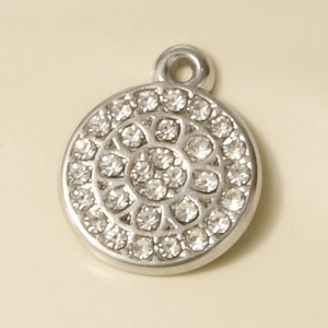 Close-up of a silver circular pendant with sparkling rhinestone inlay on beige background