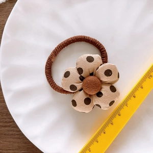 Brown floral hair tie with polka dots on a white plate with a ruler for size reference