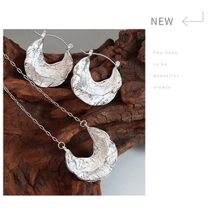 Macro detail of irregular hammered texture silver necklace and earring set on wood