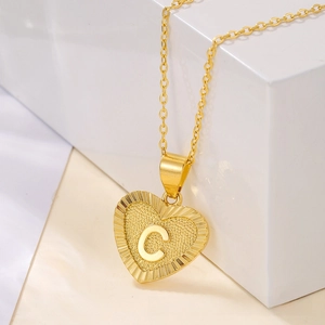 Close-up of gold heart pendant necklace with engraved letter C on minimalist stand