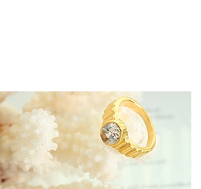 Close-up of golden grooved ring band featuring a large round-cut clear zircon stone
