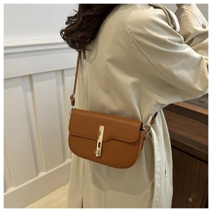 Detail shot of brown saddle crossbody bag with a gold metal lock on beige coat