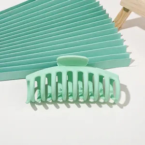 Macro detail of large mint green matte hair claw clip on harmonic paper background