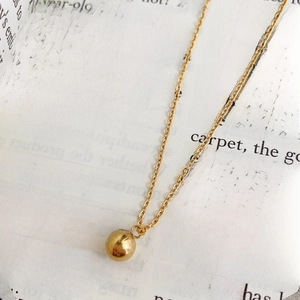 Détail macro du collier avec pendentif boule en titane doré sur fond de livre