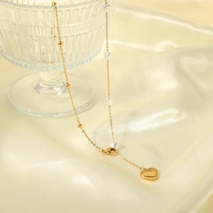 Gold heart pendant necklace with white pearls draped over a silk fabric background