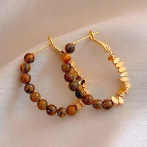 Detail of 18k gold plated hoop earrings featuring brown tiger eye beads on beige fabric