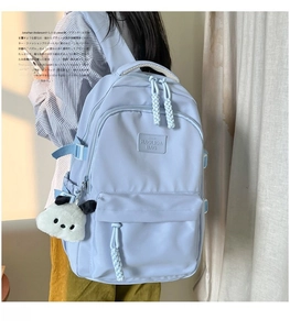Detail of light blue school backpack with side buckles and panda plush pendant