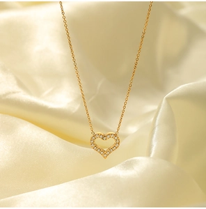 Close-up of 18K gold stainless steel hollow heart pendant with zircons on beige silk