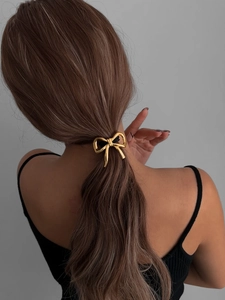 Detail of a golden bow alloy hair tie worn on a ponytail for a stylish back view