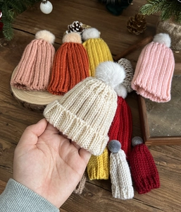Detailed knit texture of mini Christmas hats in assorted colors with fuzzy pom-poms