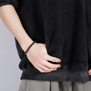 Detail of a black industrial style chain bracelet worn on a wrist with a dark hoodie