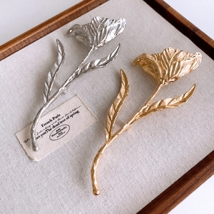 Detailed view of gold and silver tulip brooches with textured metal petals on linen