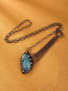Close-up of blue teardrop labradorite pendant with vintage bronze chains and tassels