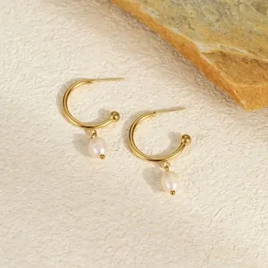 Macro detail of French style gold hoop earrings with white pearls on a stone background