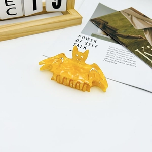 Close-up of amber bat hair claw clip on a white desk with aesthetic lifestyle props