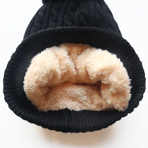 Detailed macro shot of black cable-knit beanie with soft beige fleece lining for winter