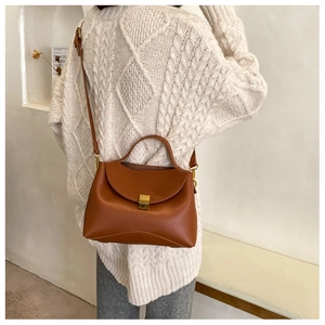 Detail of a brown PU leather handbag with a gold lock and thin strap against a knit sweater