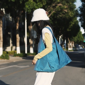 Blue oversized slouchy tote bag with pleated texture shown in an outdoor lifestyle setting