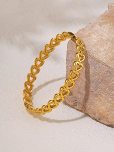 Detailed view of hollow heart pattern bangle with 18K gold plating on a natural stone