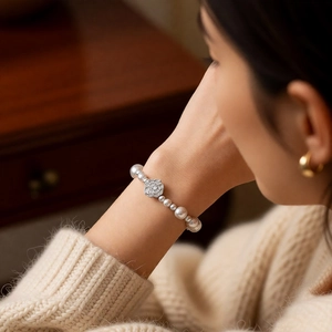 Detailed view of pearl bead bracelet with silver flower charm on a model's wrist
