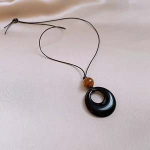 Detail of hollow round resin pendant with textured brown bead on smooth pink silk