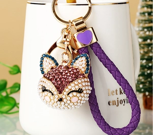 Close-up of a fox keychain with pink rhinestones and a purple braided leather strap