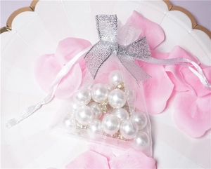 Macro shot of transparent mesh jewelry bag with white pearls and silver ribbon bow