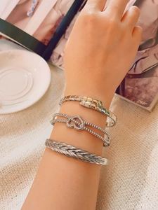Detail of silver bangles featuring snake bone, heart charms, and leaf texture
