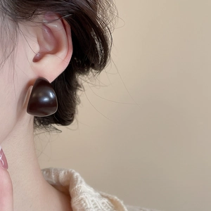 Close-up of minimalist dark brown C-shaped acrylic stud earrings worn on ear