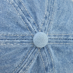 Detailed top view of light wash denim baseball cap with stitched panels and button