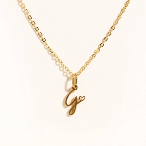 Detailed close-up of golden necklace with initial J pendant and small heart charm