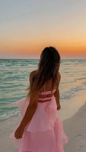 Detail of a pink backless tiered chiffon dress fluttering against a seaside sunset backdrop