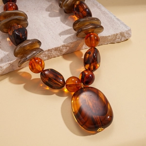 Macro shot of amber resin beads and large pebble pendant on textured stone background