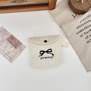 Dettaglio della pochette trapuntata color crema con fiocco nero e ricamo elegante