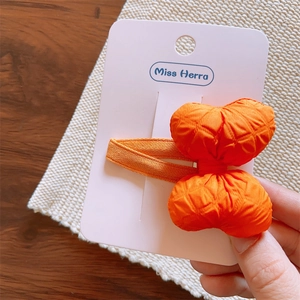 Detail of orange quilted fabric bow hair clip on a display card held by hand
