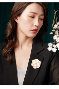 Détail de la broche camélia avec éclat nacré et bordure dorée sur un blazer noir