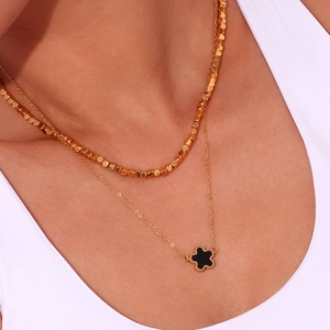 Detail of double-layer gold necklace featuring cubic beads and a black floral pendant