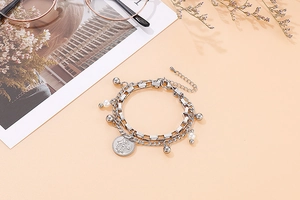 Detail view of silver double-layer hamsa hand bracelet with pearls on a beige surface