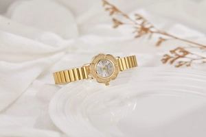 Gros plan du cadran doré en forme de fleur et du bracelet en acier de cette montre