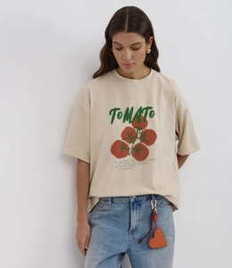 Λεπτομέρεια από μπεζ oversized T-shirt με κόκκινο τύπωμα ντομάτας και πράσινο κείμενο