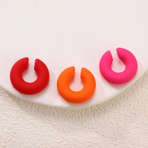 Detailed macro shot of three matte C-shape acrylic ear clips in red, orange, and pink colors