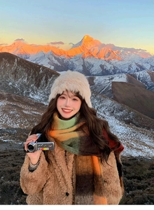 Close-up of rainbow plaid scarf and white plush hat set against a snowy mountain background