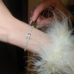 Detail of a tennis bracelet featuring a pink emerald-cut stone with gold plating