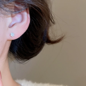 Close-up of minimalist four-prong silver stud earring with clear sparkling zircon stone