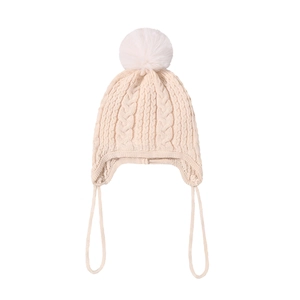 Close-up of knit baby winter hat in creamy white with earflaps and a fuzzy pom-pom