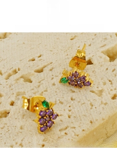 Macro shot of grape-shaped earrings with purple gems and green leaf on gold titanium steel