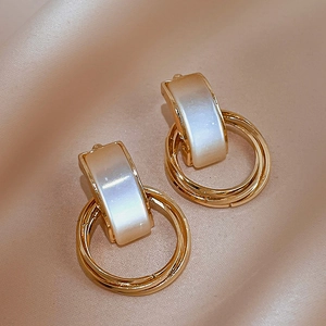 Detailed close-up of golden metal earrings with white faux cat-eye stone on silk fabric