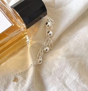 Detailed view of silver 925 beaded bracelet with heart pendant on soft beige fabric