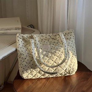 Vue détaillée du sac cabas matelassé beige à motifs de cœurs noirs sur un tabouret